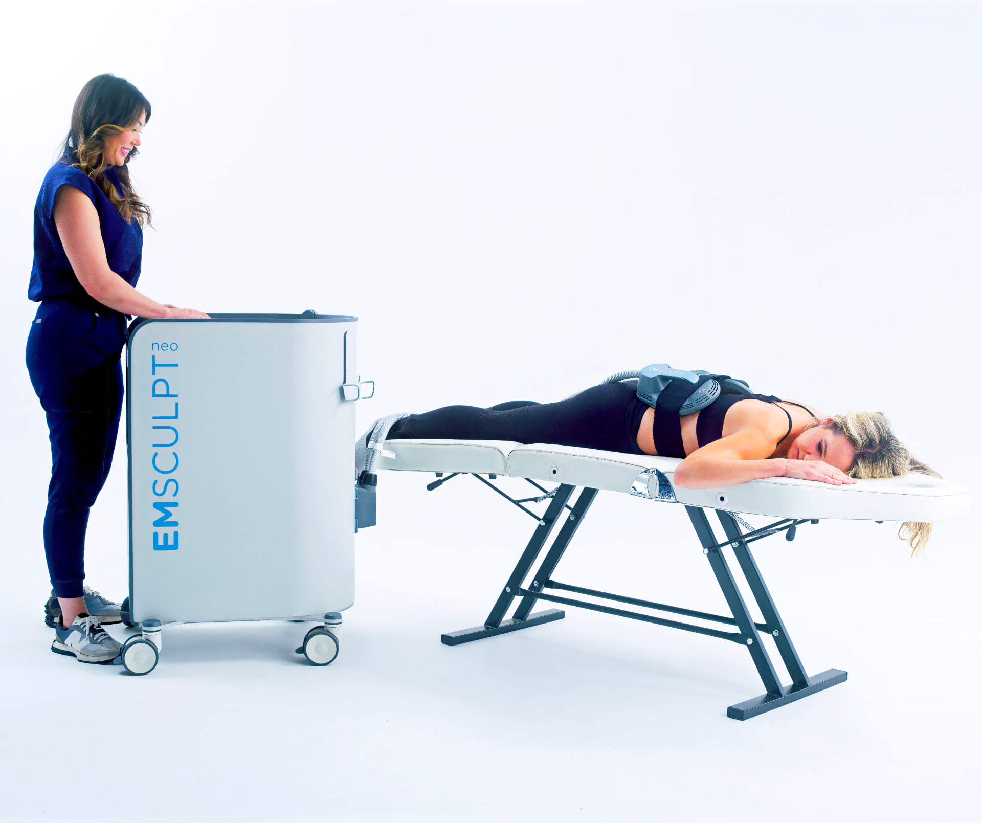 Emsculpt NEO treatment: a clinician stands beside the device while an applicator paddle rests on a client's lower back during a session